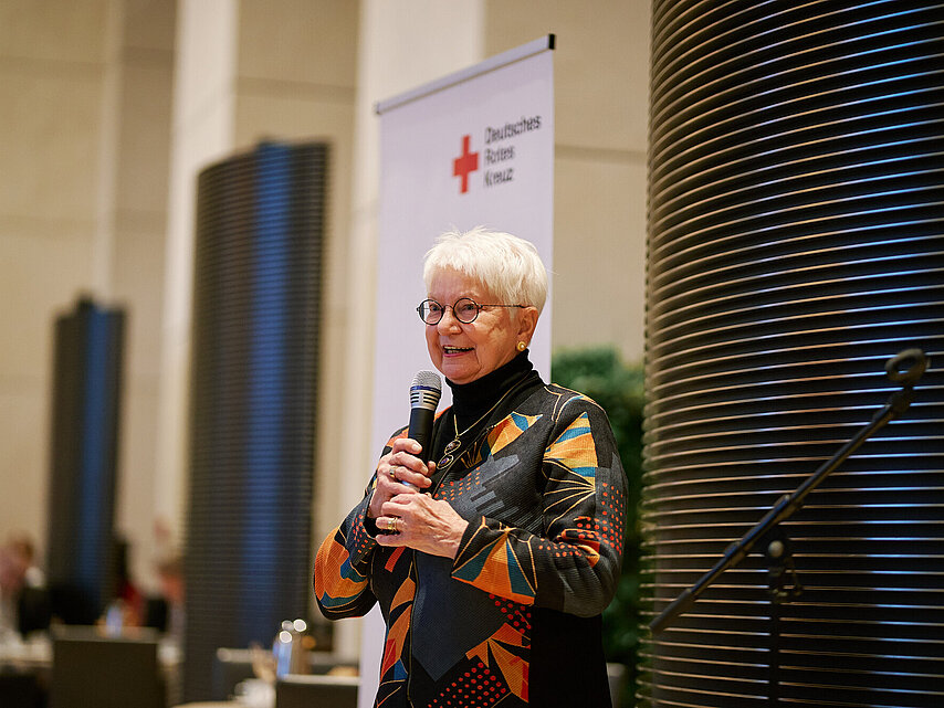Frau Hasselfeldt, Präsidentin des DRK, steht mit einem Mikrofon vor mehreren Bannern.