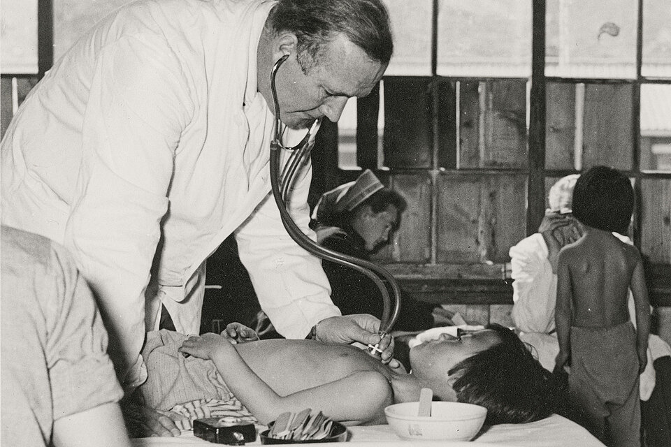 Arzt untersucht liegendes Kind mit Stethoskop