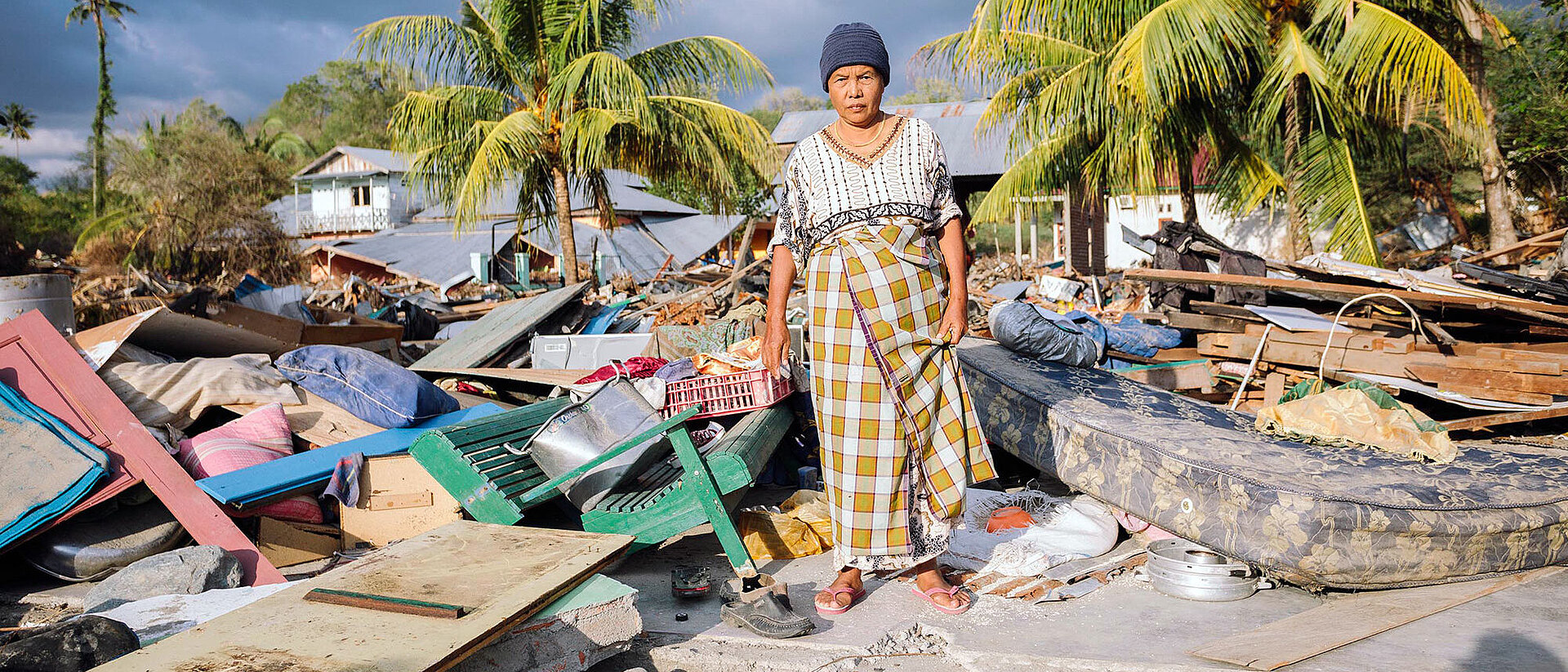 Seniorin steht auf Trümmern vor Palmen
