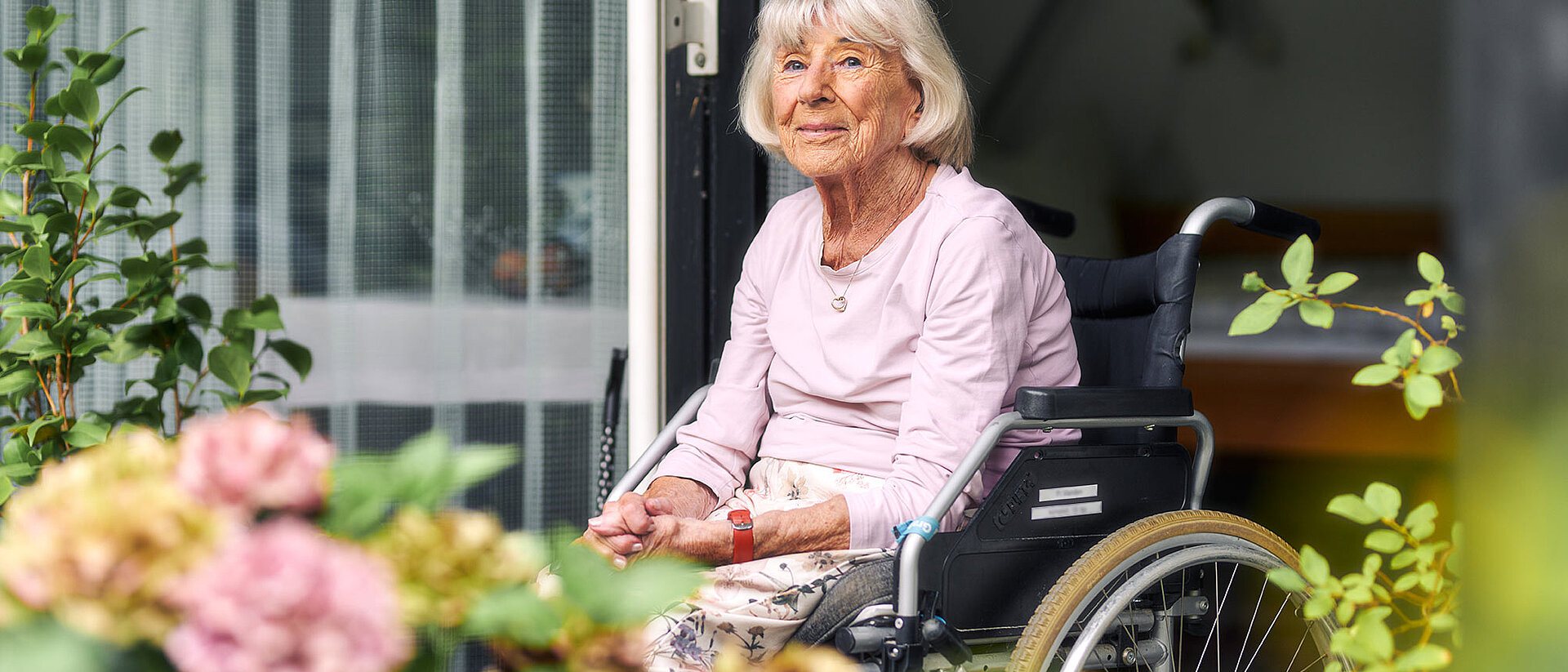 Seniorin im Rollstuhl auf Balkon mit Blumen