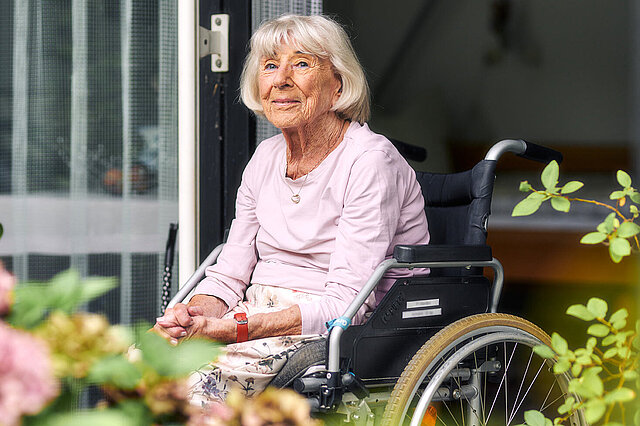 Seniorin im Rollstuhl auf Balkon mit Blumen