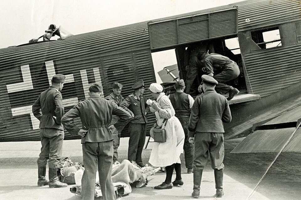 Schwerverwundeter und Helfer vor Flugzeug