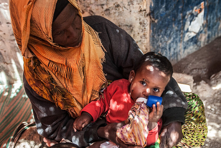 Foto: Ein somalisches Baby mit Flasche auf dem Schoß einer Angehörigen
