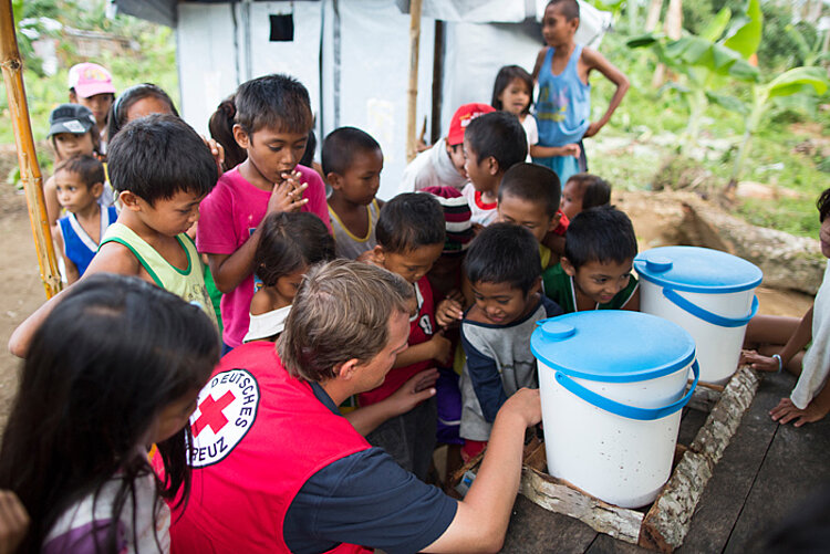 DRK-Helfer und philippinische Kinder vor zwei Wassereimern
