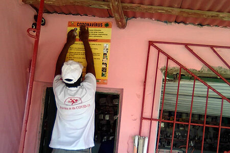 Umgang mit Katstrophen: Mosambikanerin bringt Covid-19-Plakat über Tür an
