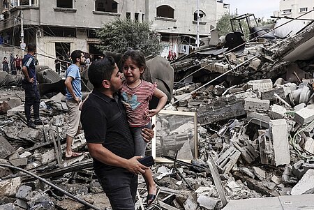 Mann trägt ein weinendes Kind und läuft über zerstörte Gebäude