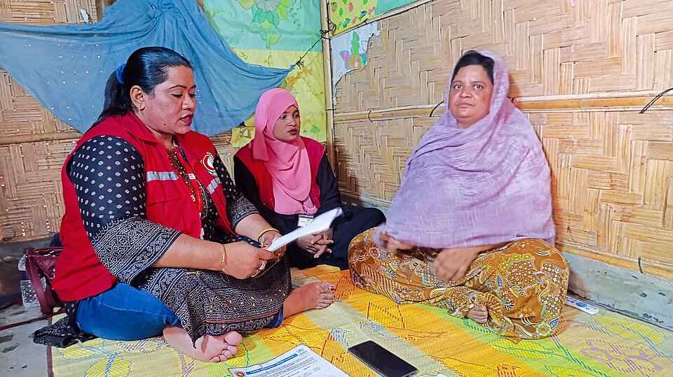 In einer Unterkunft sitzen zwei Freiwillige des BDRCS und die Bewohnerin im Gespräch