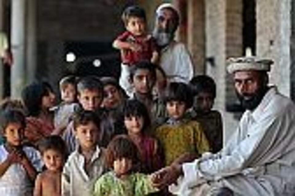 Foto: Eine Gruppe Flüchtlingskinder in Pakistan, recht und im Hintergrund ältere Männer