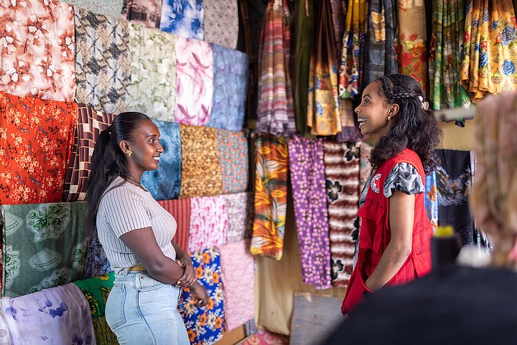 Rotkreuzlerin im Gespräch mit Schneiderin vor Stoffen