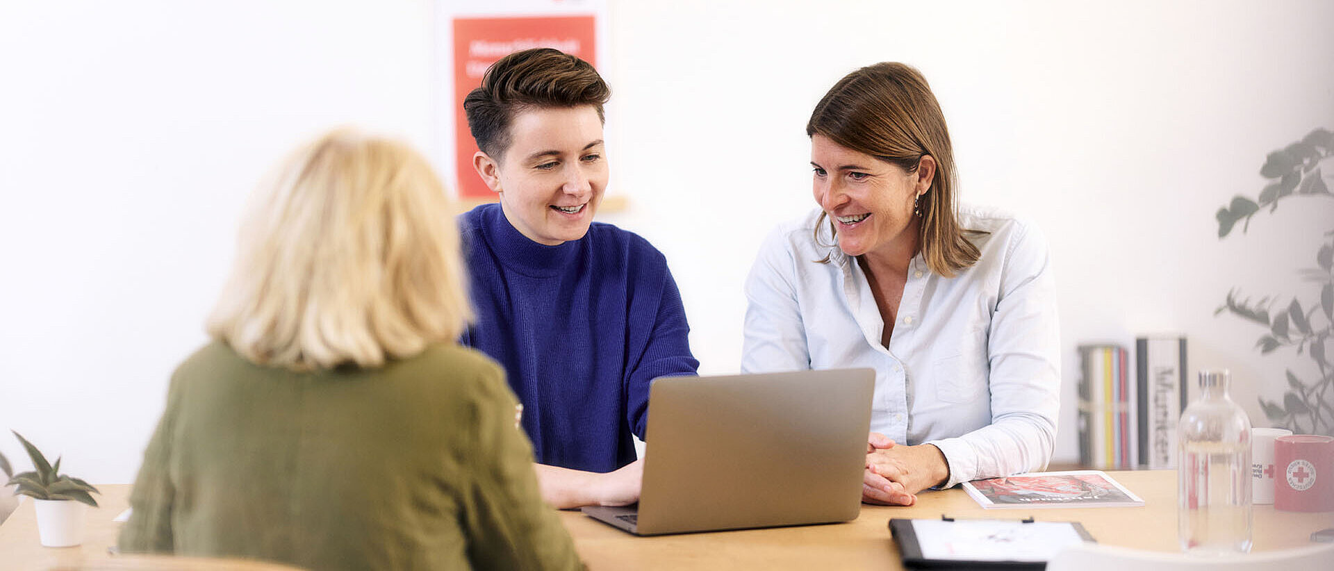 Drei Frauen lächelnd im Gespräch am Laptop