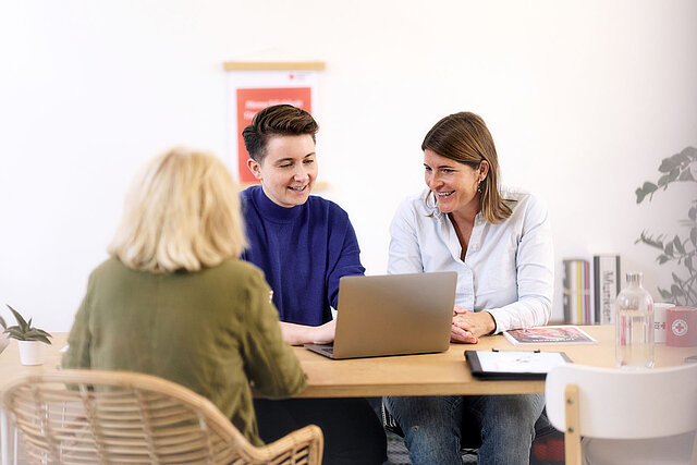 Drei Frauen lächelnd im Gespräch am Laptop