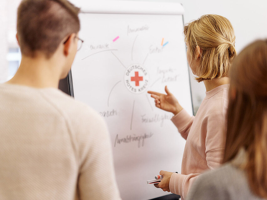 Drei Personen betrachten Flipchart mit DRK-Logo