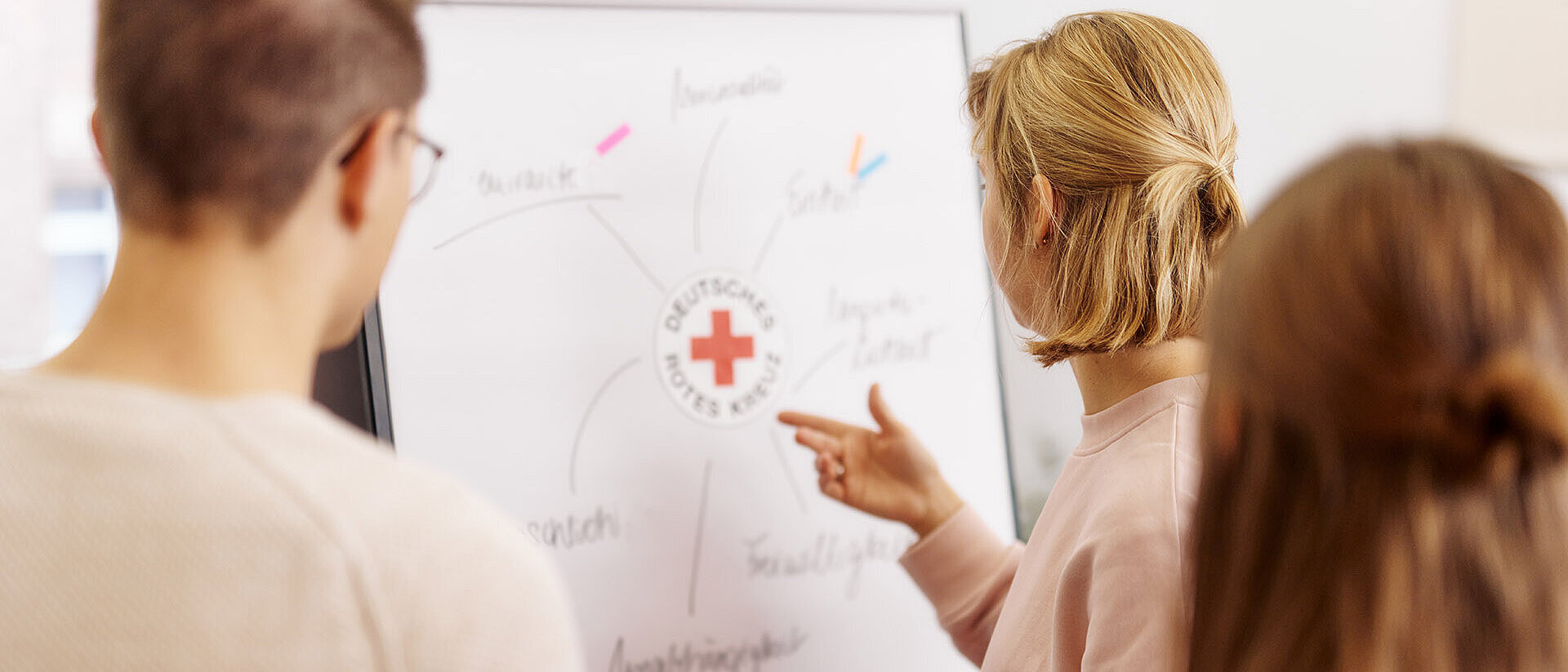 Drei Personen betrachten Flipchart mit DRK-Logo