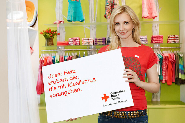 Foto: Jette Joop vor Kinderkleidung mit Spruchschild im Arm.