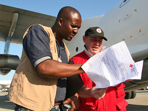 Foto: DRK-Mitarbeiter und ein Mitarbeiter des Haitianischen Roten Kreuzes kontrollieren vor einem Hilfsflugzeug die Fachtpapiere