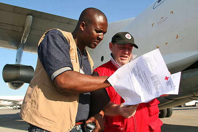 Foto: DRK-Mitarbeiter und ein Mitarbeiter des Haitianischen Roten Kreuzes kontrollieren vor einem Hilfsflugzeug die Fachtpapiere