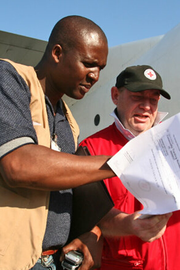 Foto: DRK-Mitarbeiter und ein Mitarbeiter des Haitianischen Roten Kreuzes kontrollieren vor einem Hilfsflugzeug die Fachtpapiere