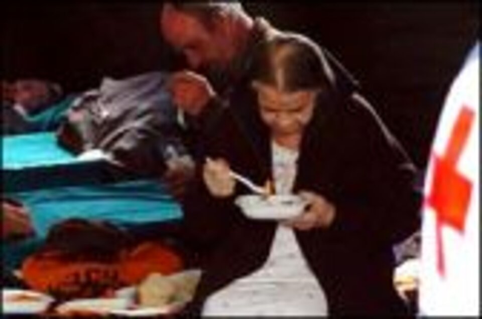 Foto: 2 Menschen essen mit einer Plastikgabel aus einer Plastikschüssel, Rotes Kreuz im Vordergrund