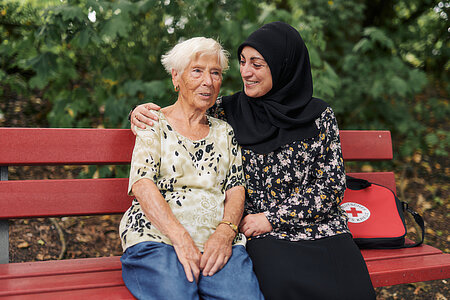 Älterer Mensch sitzt zusammen mit Person mit Kopftuch freundschaftlich auf einer Bank