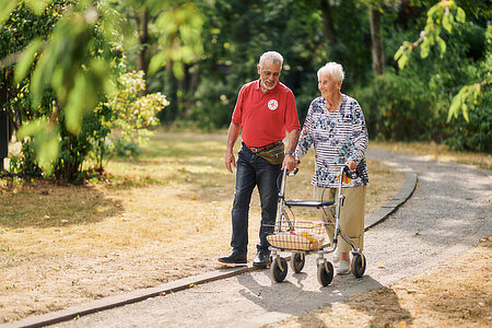 Bewohnerin eines Seniorenzentrums und DRK-Mitarbeiter beim Spaziergang