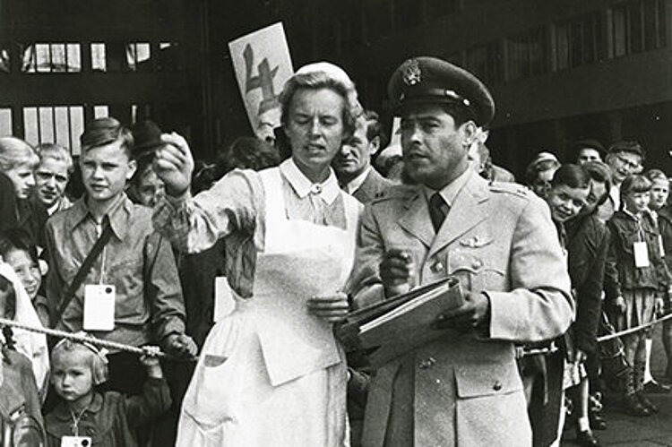 Eine Gruppe Kinder mit einer Betreuerin vom DRK und einem Offizier der US-Luftwaffe auf dem Flughafen Berlin-Tempelhof vor dem Abflug (Paul Wittig/ DRK)