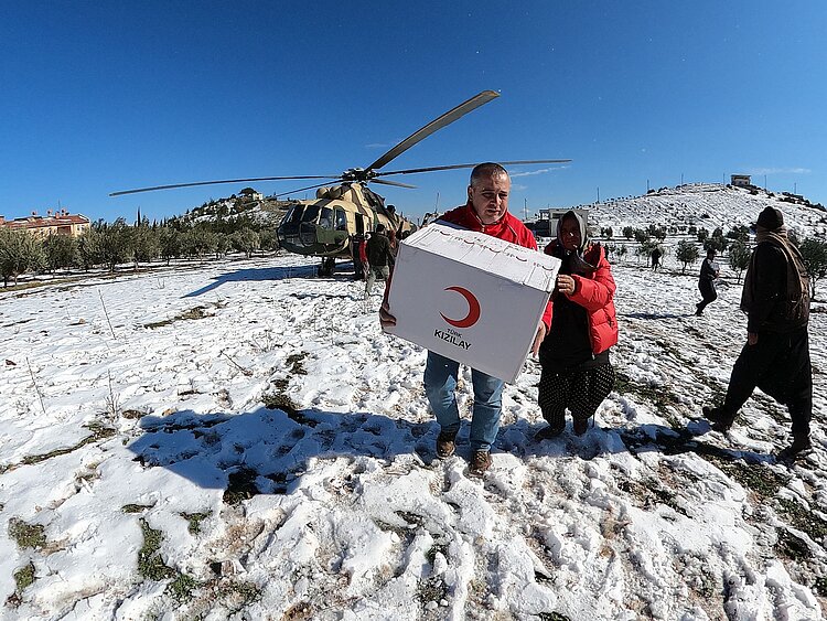 Helfer des Türkischen Roten Halbmonds trägt ein Hilfspaket durch den Schnee, nachdem die Hilfsgüter von einem Helikopter angeliefert worden sind.