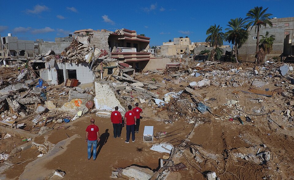 Ausblick auf ein Gebiet mit völlig zerstörten und Helfern des Libyschen Roten Halbmonds im Vordergrund
