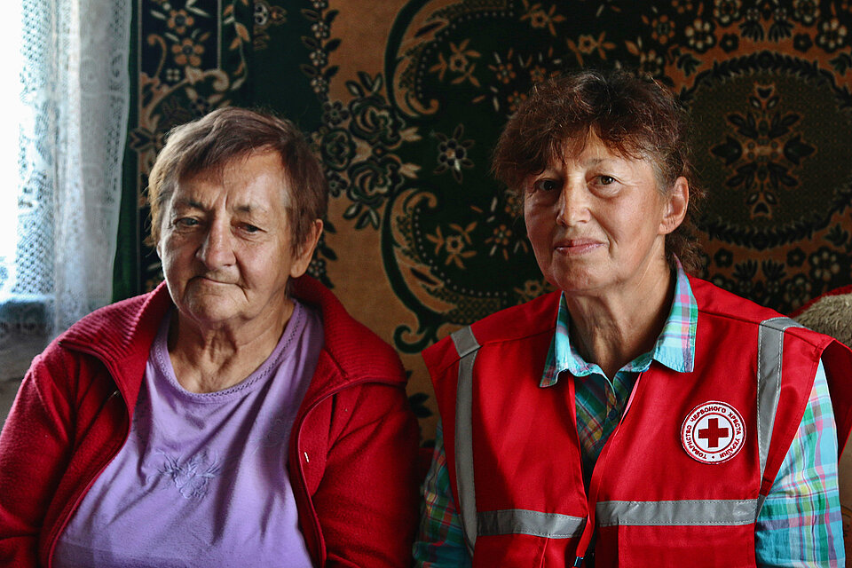 Eine ältere Frau und eine Ukrainische Rotkreuzhelferin sitzen nebeneinander und lächeln