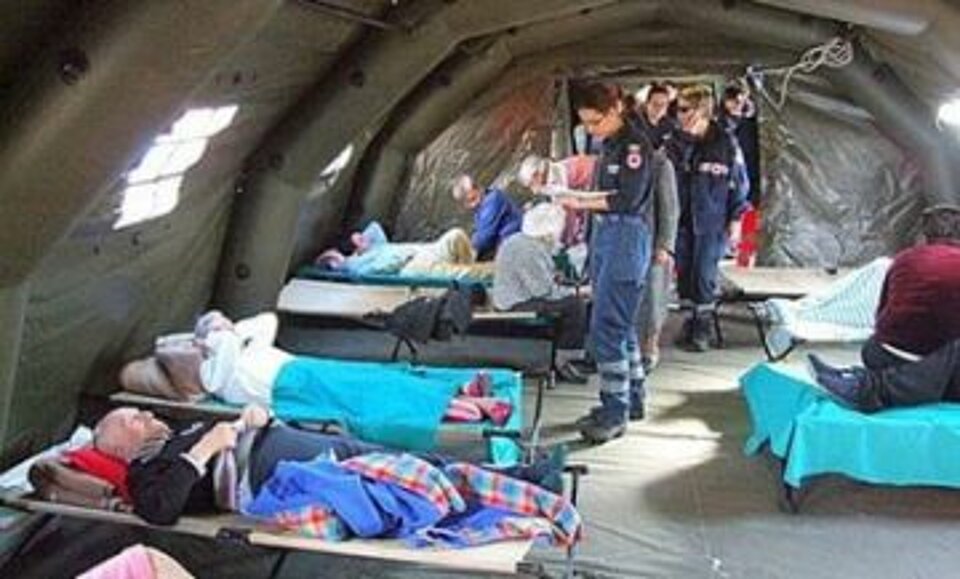Foto: ältere verletzte Menschen lieben auf Feldbetten in einem Zelt der Gesundheitsstation, Visite der Rotkreuz-Rettungskräfte