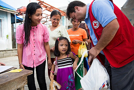 DRK-Helfer gibt eine Hilfsgütertasche an eine junge philippinische Familie