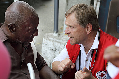 Foto: DRK-Delegierter spricht mit einem älteren Mann in Haiti.