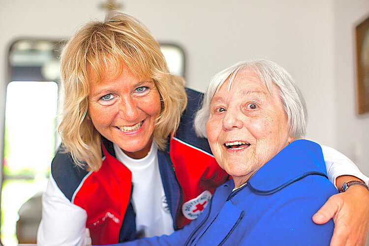 lächelnde Pflegerin legt Arm um Seniorin