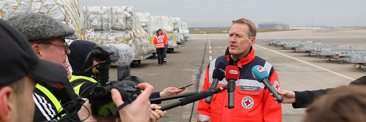 DRK-Generalsekretär Christian Reuter steht in DRK-Einsatzkleidung im Freien und wird interviewt