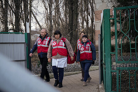 Mitarbeitende des Ukrainischen Roten Kreuzes gehen im Winter zu einem Einsatz in einem ländlichen Gebiet. Alle vier Personen tragen rote Westen.