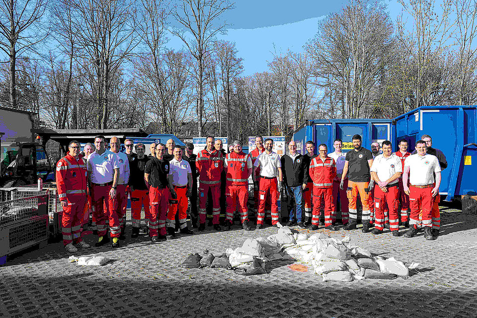 Zahlreiche Männer stehen in DRK-Kleidung im Freien. 