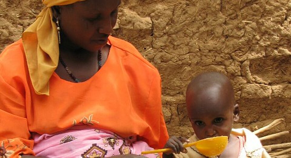 Foto: ein unterernährter kleiner nigerischer Junge löffelt Brei.