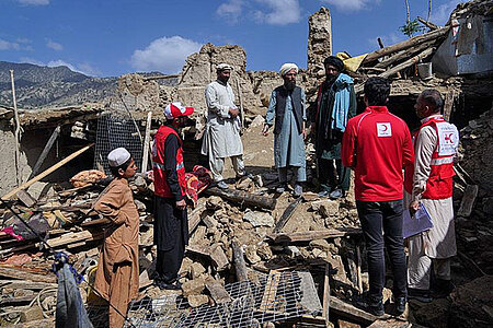 Männer stehen mit Helfern auf Erbbebentrümmern in Afghanistan