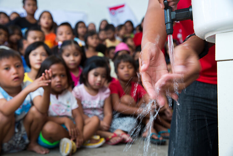 Vor einer Gruppe Kindern wäscht sich ein DRK-Helfer die Hände