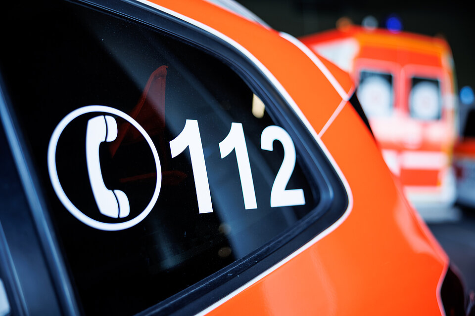 Auto mit der 112 in der Autoscheibe. Im Hintergrund ein Rettungswagen.