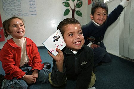 Drei lernende Kinder, die sich lachend melden