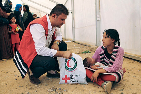 Foto: Irakischer Rothalbmondhelfer überreicht einem Mädchen mit einem Baby auf dem Schoß einen Hilfsgüterbeutel