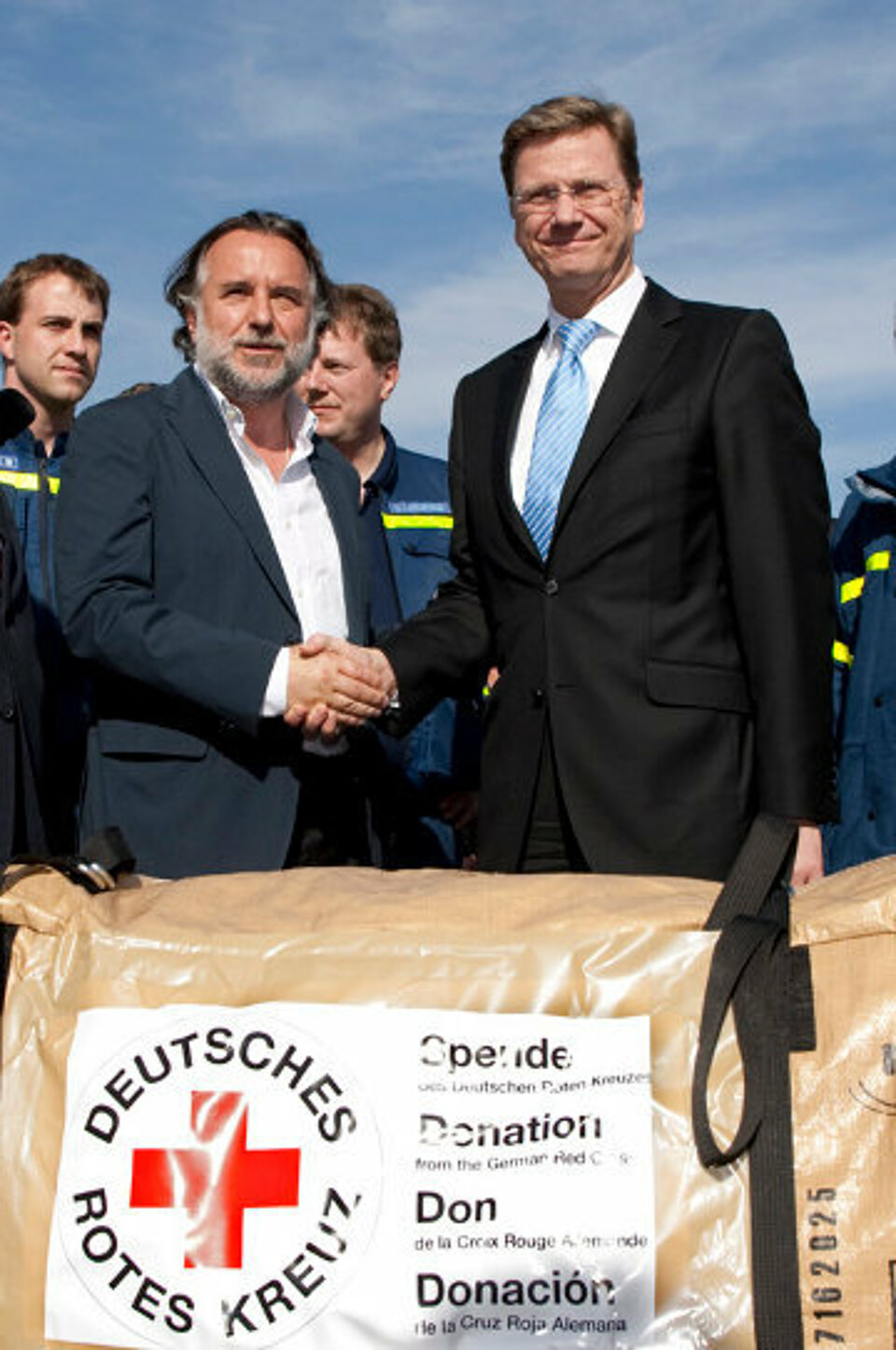 Foto: Guido Westerwelle und Mariano Fernándezschütteln sich vor Hilfsgütern des DRK die Hand.