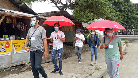 Rotkreuz-Freiwillige mit roten Regenschirmen auf Fußweg