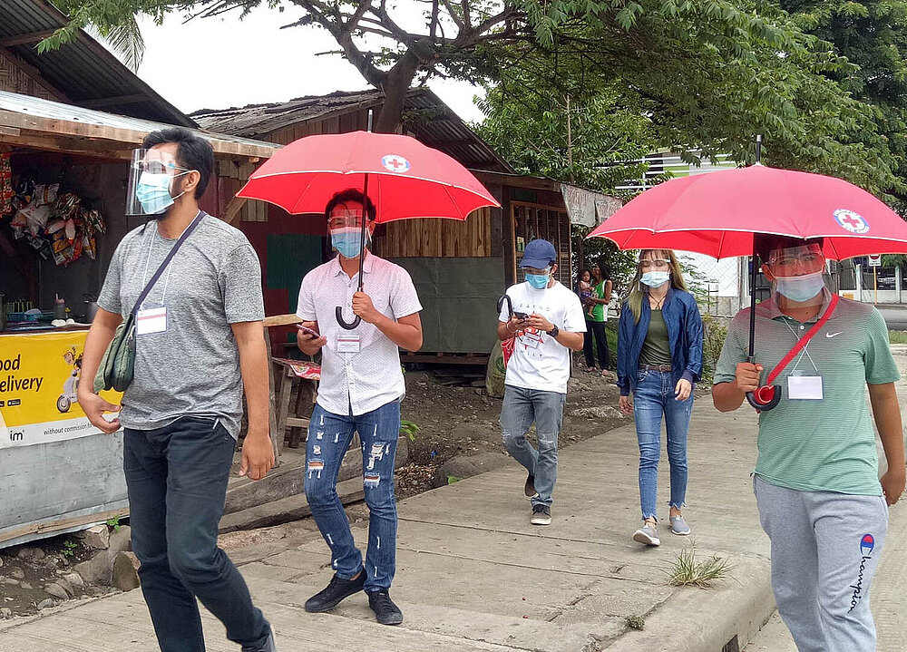 Rotkreuz-Freiwillige mit roten Regenschirmen auf Fußweg