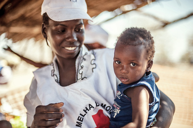 Foto: Helferin des Mosambikanischen Roten Kreuzes mit einem Kleinkind auf dem Arm