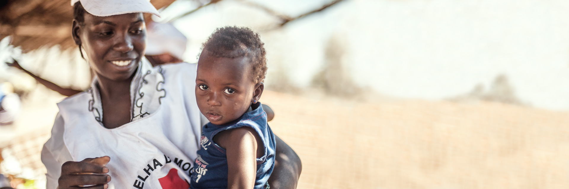 Foto: Helferin des Mosambikanischen Roten Kreuzes mit einem Kleinkind im Arm