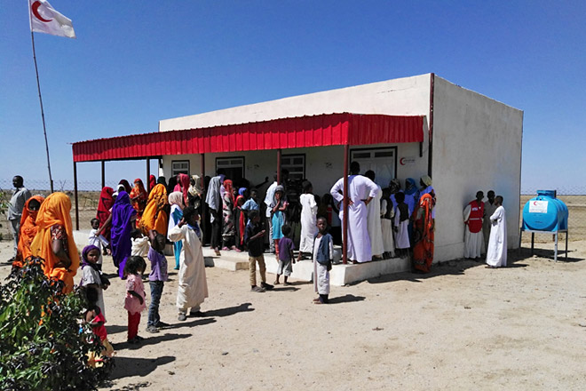 Foto: Sicht auf eine Erste-Hilfe-Sation im Sudan mit davor wartenden Menschen