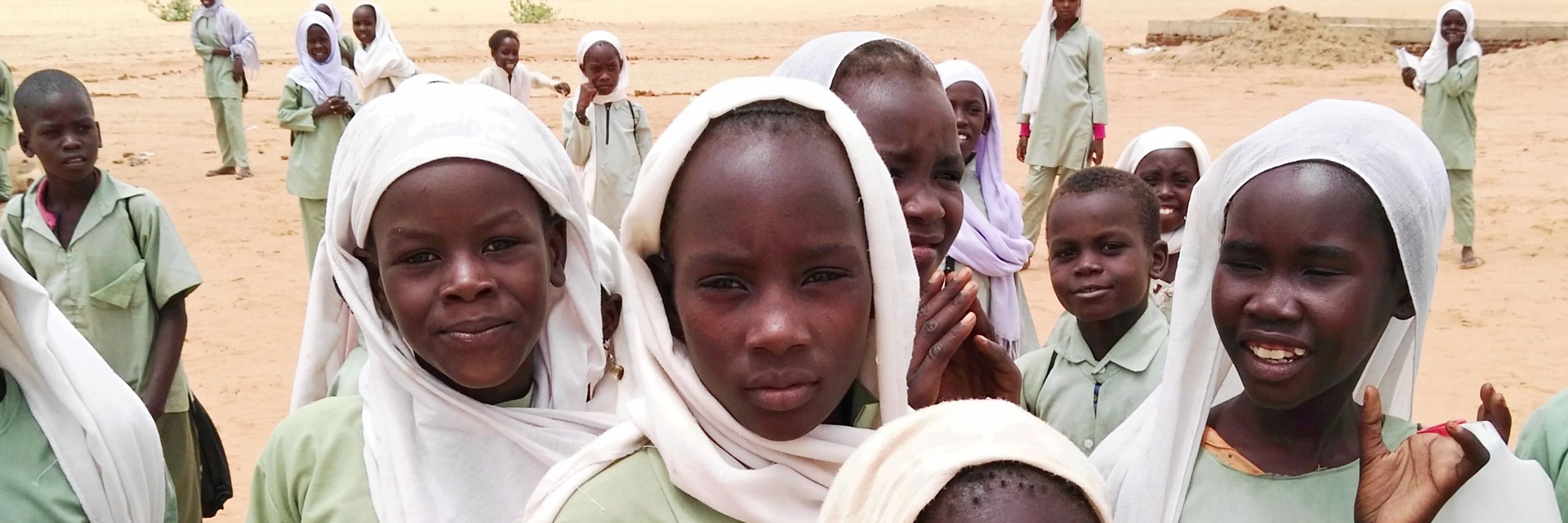 Foto: Schülerinnen auf einem Sandplatz im Sudan
