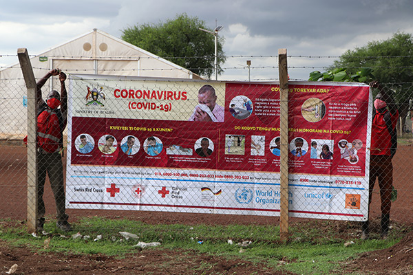 zwei ugandische Rotkreuzler hängen Projektplakat der Hygiene-Kampagne auf