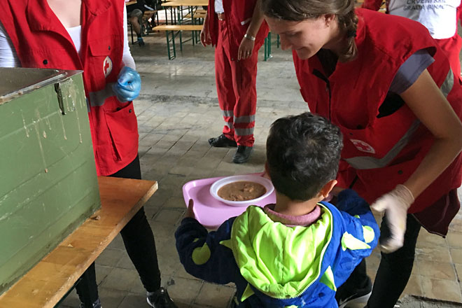 Foto: Rotkreuzhelferin reicht Kind ein warmes Essen auf einem Tablett (Flüchtlingslager Bosnien-Herzegowina) 